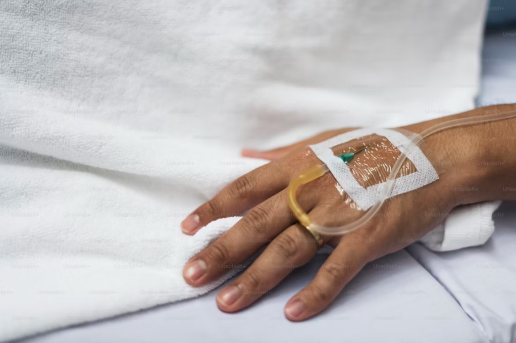 Close-up of a hand resting on a bed with an IV cannula taped in place, no face visible